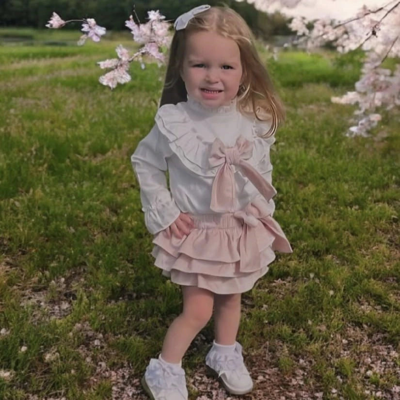 Young girl in a white and pink dress standing in a field with cherry blossoms.