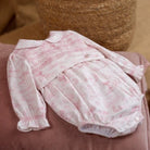 Pink baby romper with lace details on a pink surface