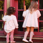 Two young girls in matching outfits standing on a porch with a red door.