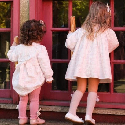 Two young girls in matching outfits standing on a porch with a red door.