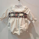 A white Santa romper with a red and ivory tartan pattern, frill collar, and a rear tartan bow, displayed on a hanger.