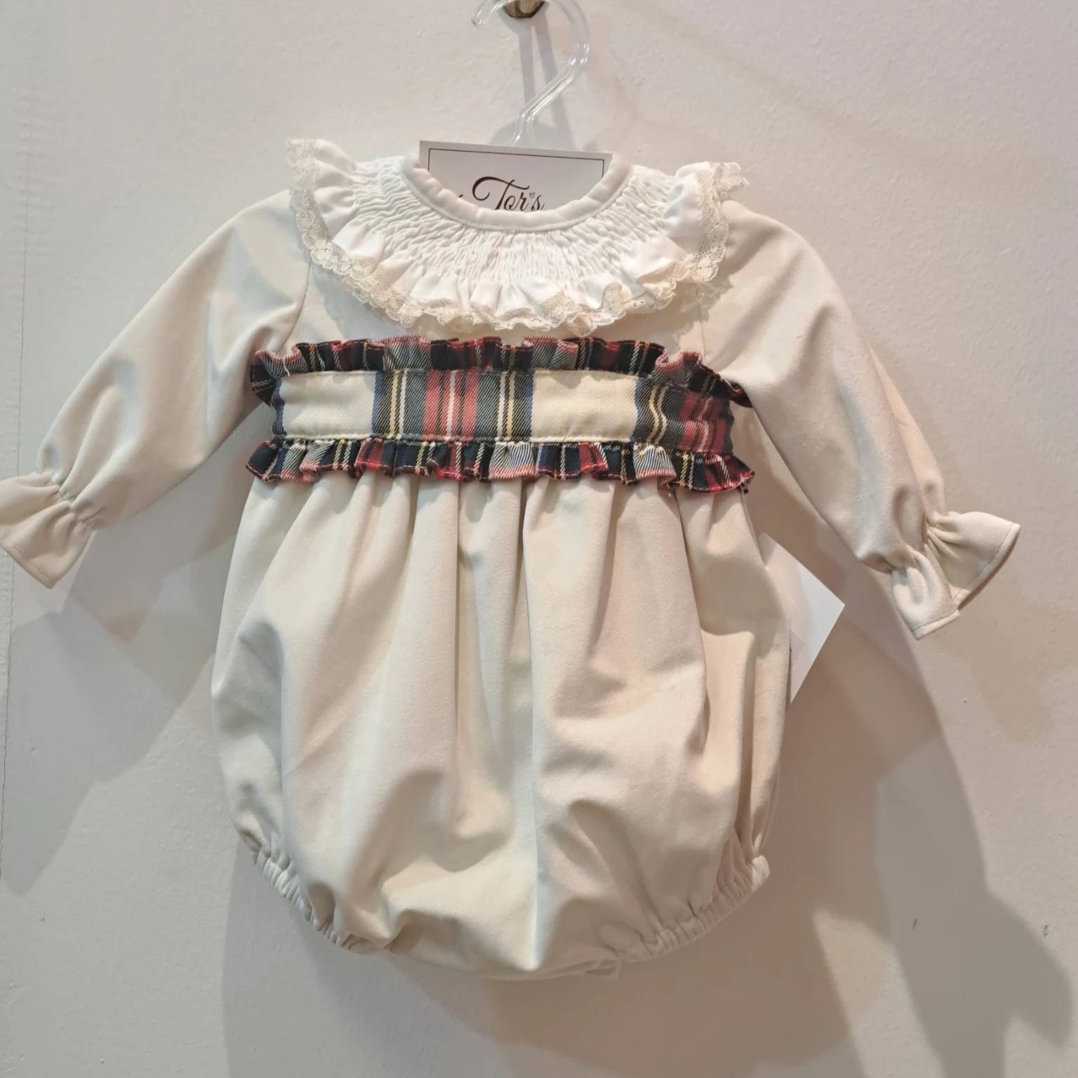 A white Santa romper with a red and ivory tartan pattern, frill collar, and a rear tartan bow, displayed on a hanger.